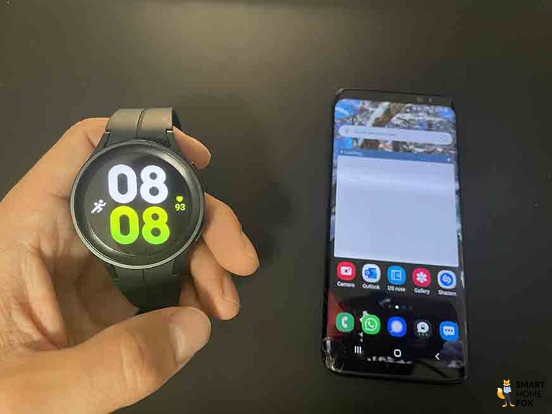 Man sieht die Galaxy Watch 5 neben einem Handy.